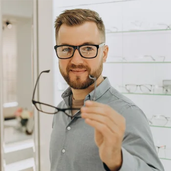 A man comparing eyeglass frames at the optometrist's office, trying to choose a pair