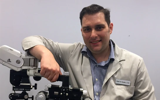 A photo of Dr. Mark Burke wearing a lab coat and posing with diagnostic equipment
